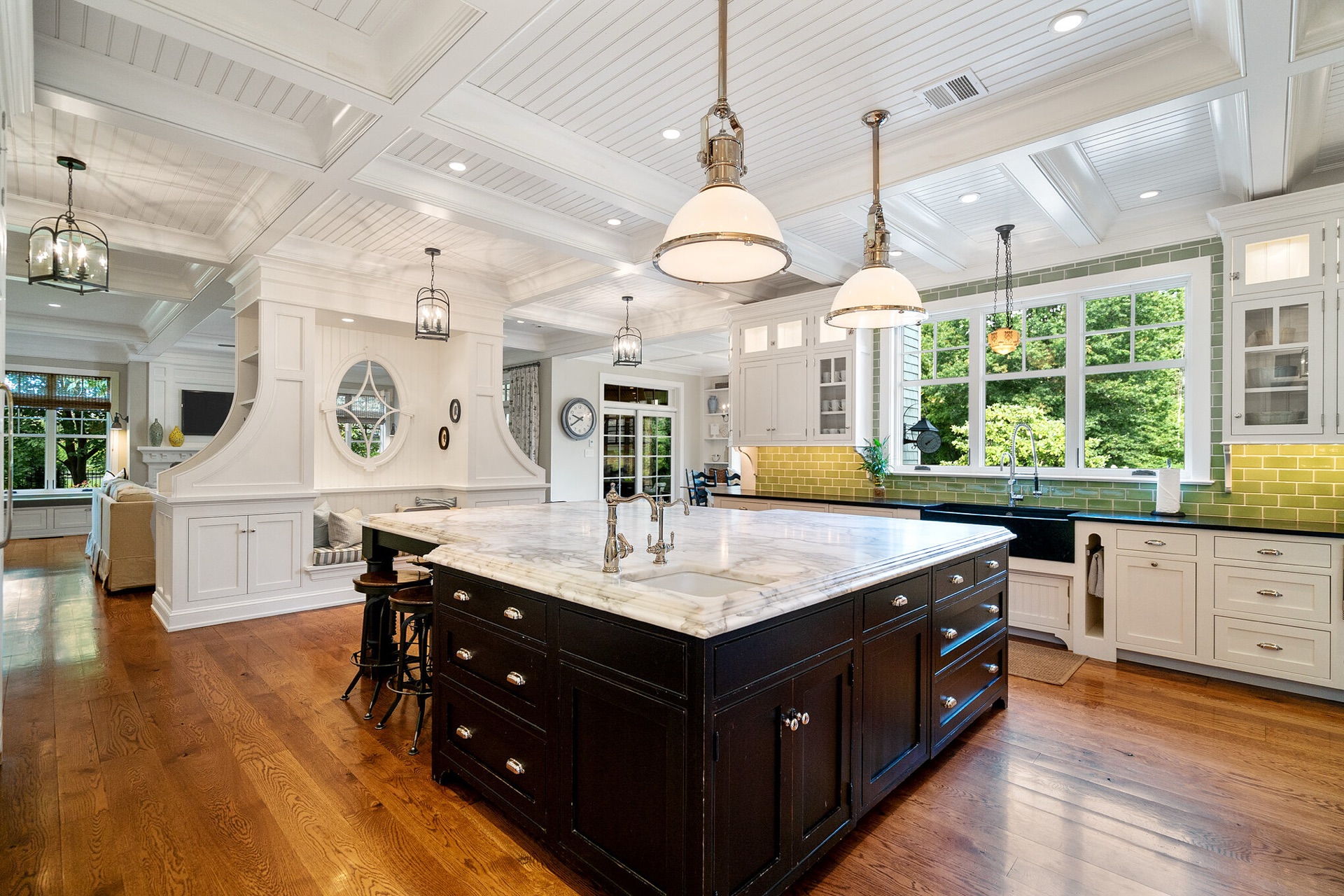 Elysian Manor kitchen and dining design with a white coffered ceiling, dark island, marble countertops and warm hardwood floors