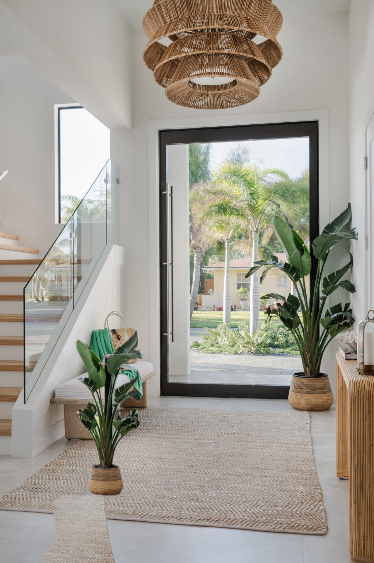 Coastal entryway designed by Oak Heart Interiors with a woven chandelier, glass stair railing and natural textures