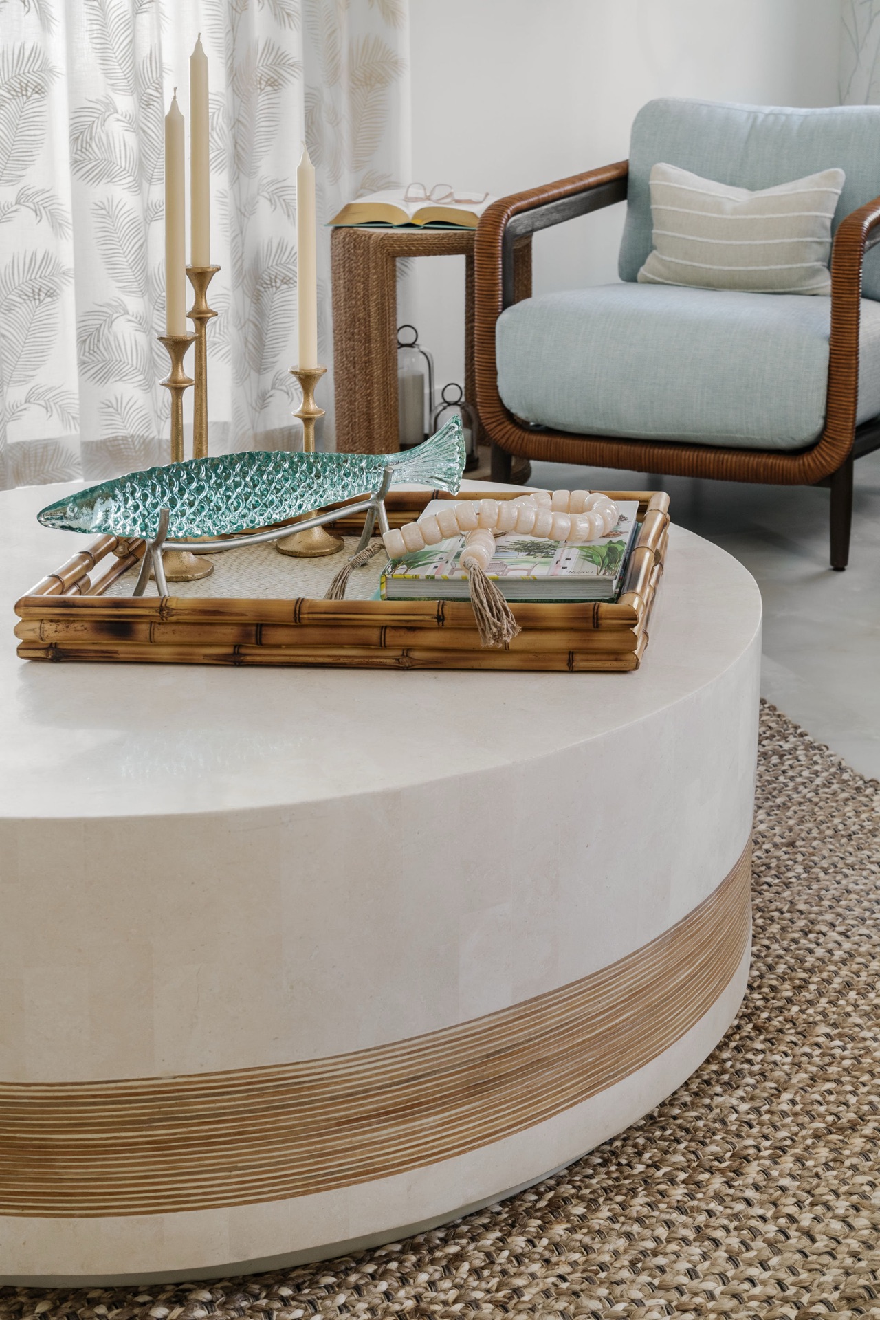 Coastal living room detail with a round travertine table, rattan chair and natural textures by Oak Heart Interiors