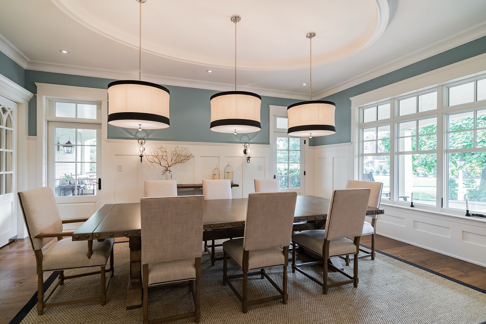 Formal dining room with soft blue walls, drum pendants and upholstered seating designed by Oak Heart Interiors