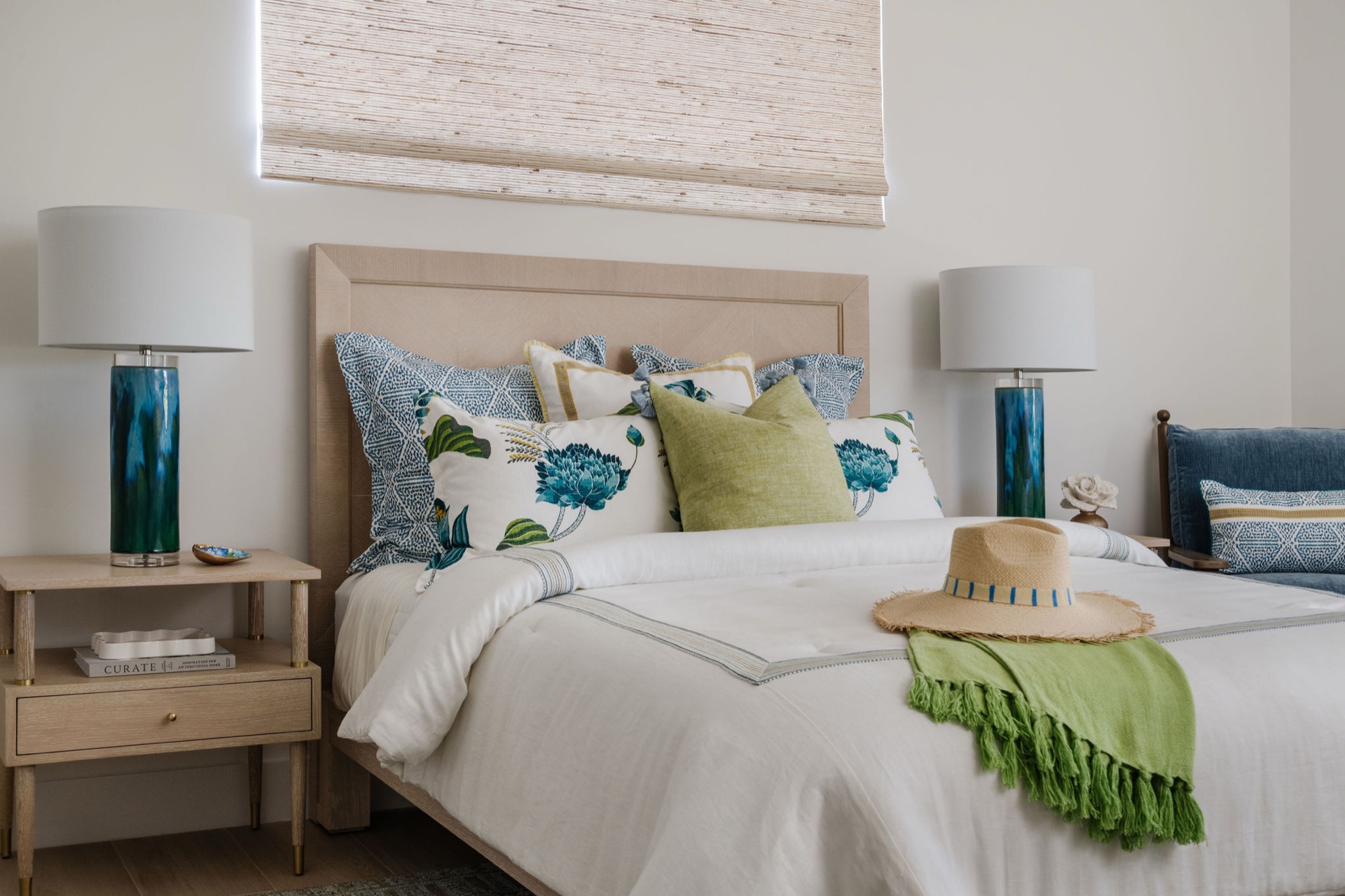 Aurora bedroom design with a woven shade, upholstered headboard and coastal blue and green accents